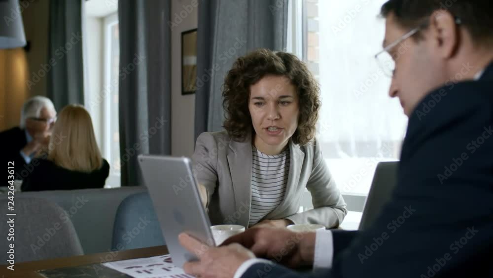 Young professional businesswoman smiling and discussing project on digital tablet with male colleague while sitting at cafe table on lunch Young professional businesswoman smiling and discussing project on digital tablet with male colleague while sitting at cafe table on lunch