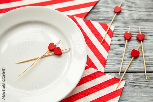 toothpicks with a small red hearts on a white plate and striped festive napkin. Close up