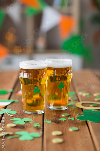 st patricks day, holidays and celebration concept - glasses of draft light beer, shamrock, gold coins and other party props on wooden table