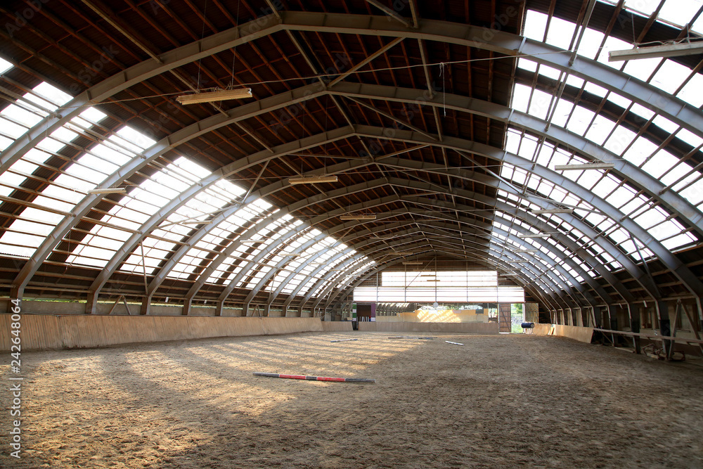 View in an empty indoor riding hall center for horses and riders. The riding school is suitable for dressage and jumping  horses