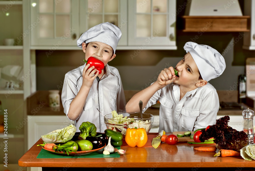 The boys in the cooks costumes cut the salad in the kitchen. Children prepare healthy food. Friendly cooperation of cooks. Eat raw vegetables. The boys in the cooks costumes cut the salad in the kitchen. Children prepare healthy food. Friendly cooperation of cooks. Eat raw vegetables.
