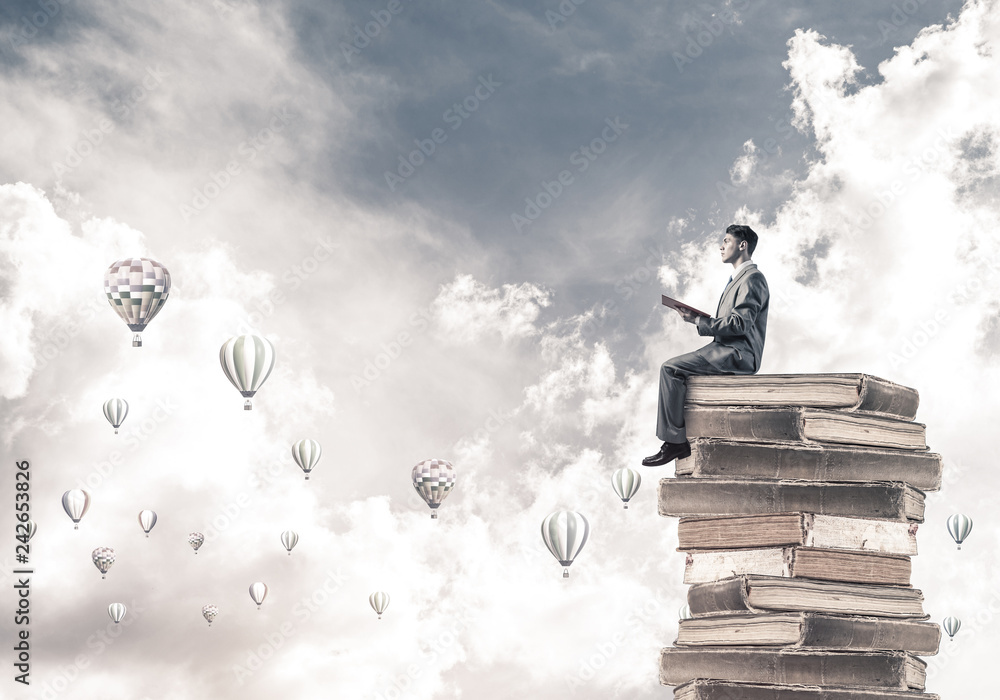 Man student reading book and aerostats flying around in air Man student reading book and aerostats flying around in air