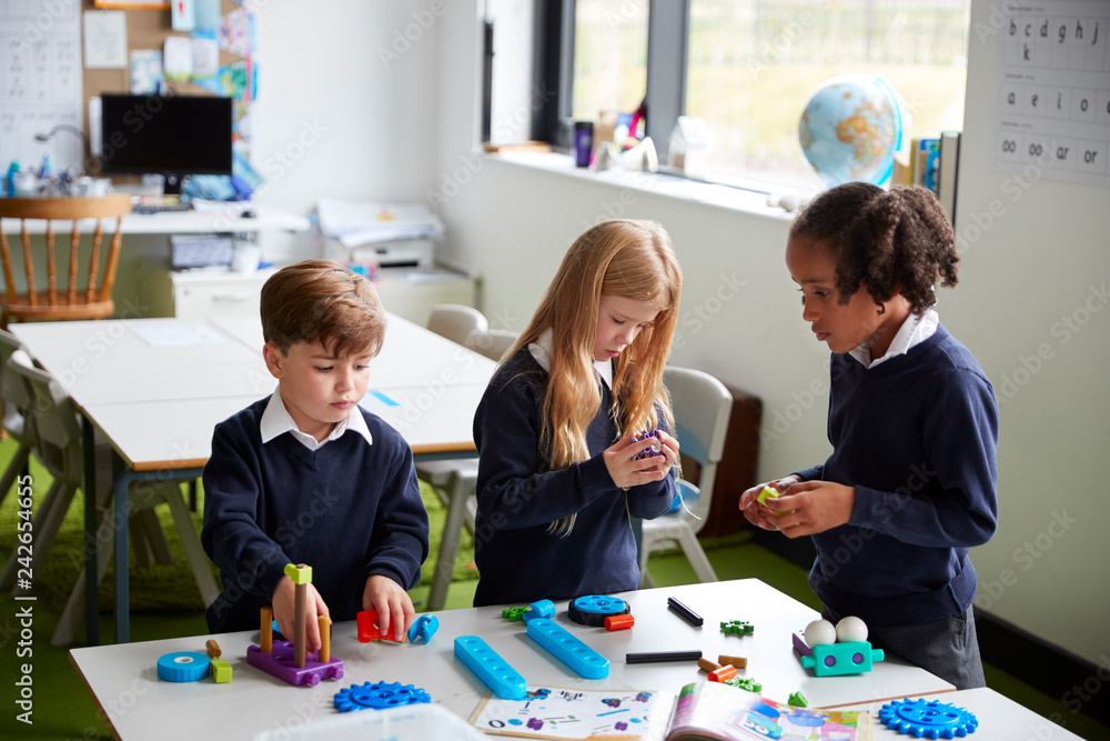 Fototapeta premium Elevated view of three primary school kids working together using construction blocks in a classroom