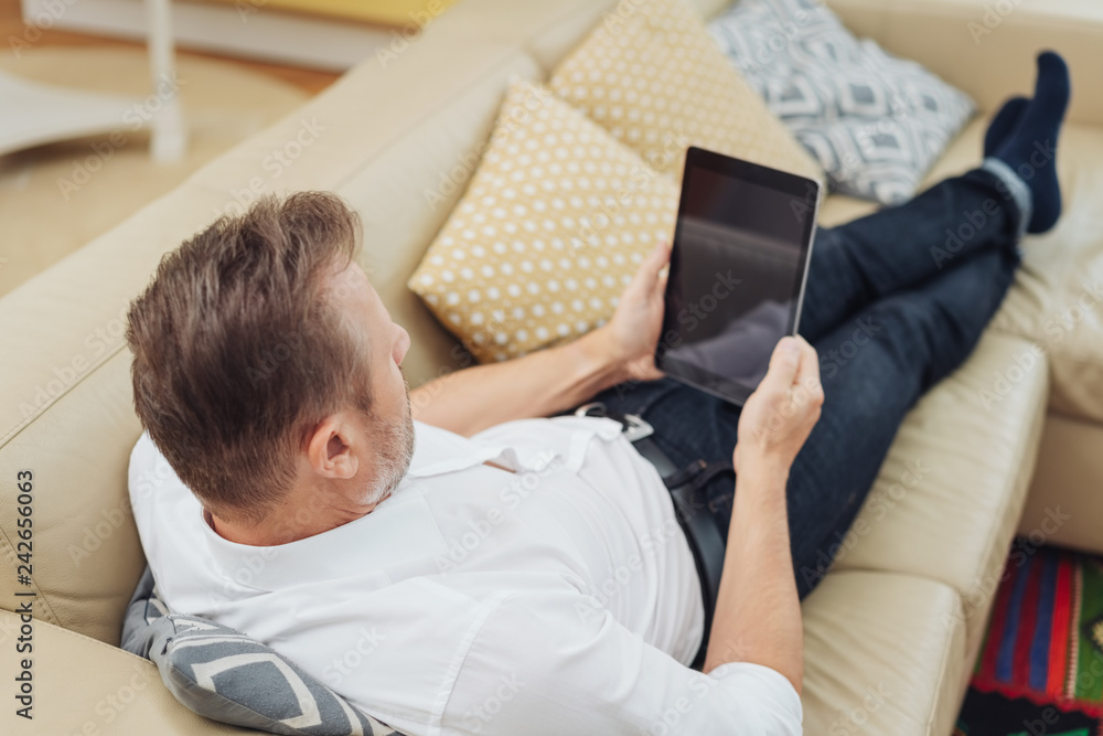 man relaxing on a sofa with a tablet man relaxing on a sofa with a tablet