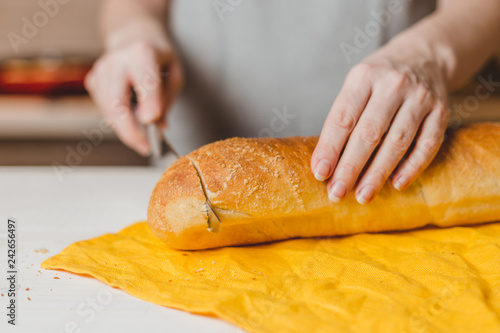 Female European hands cut fresh crisp baguette on wooden board
