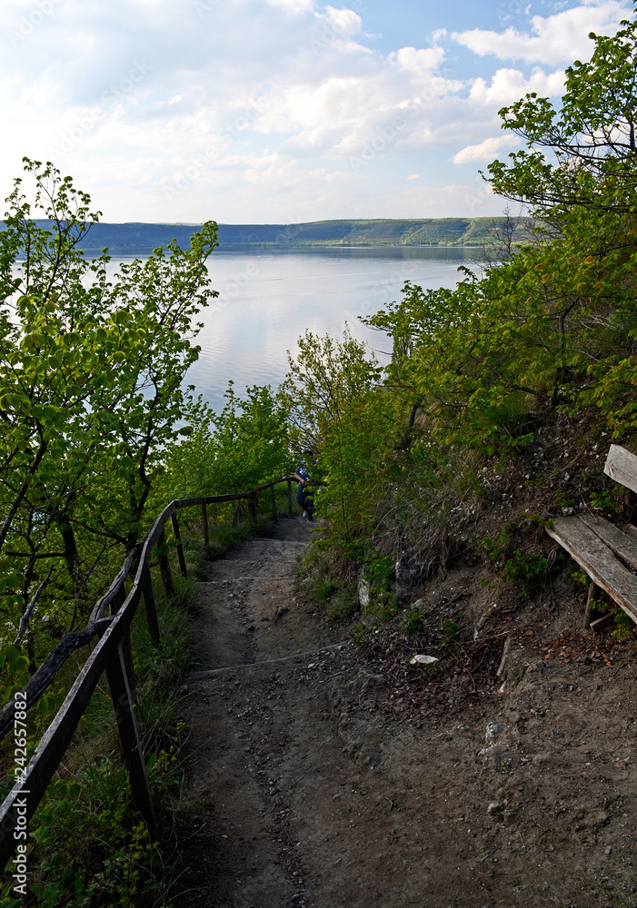 The huge river Dniester flows between high steep hills covered with spring lush green grass against the blue sky The huge river Dniester flows between high steep hills covered with spring lush green grass against the blue sky