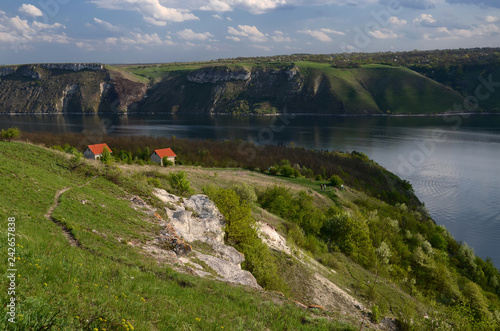 The huge river Dniester flows between high steep hills covered with spring lush green grass against the blue sky photo