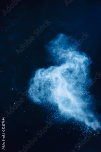 Flour powder explosion in motion. Action food photography. Light blue dust on a black background with copy space