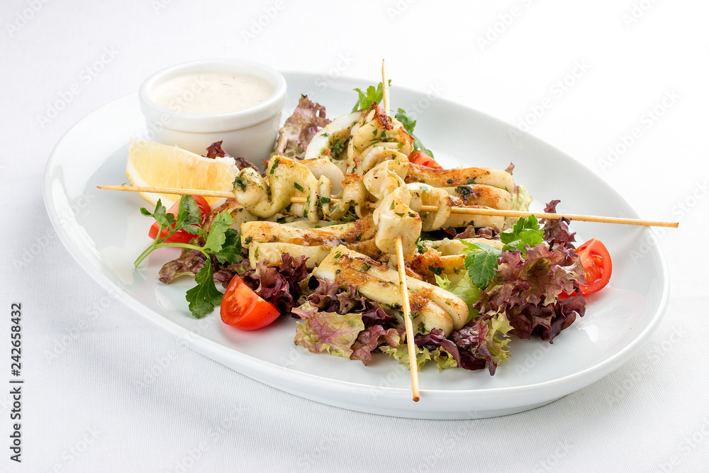 Squid grilled on skewers, with salad and sauce. On white background Squid grilled on skewers, with salad and sauce. On white background