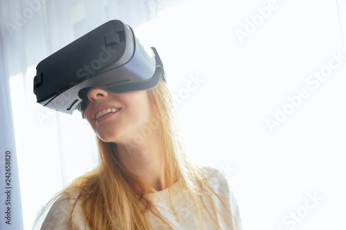 Young blonde at home with a modern design puts on virtual reality glasses