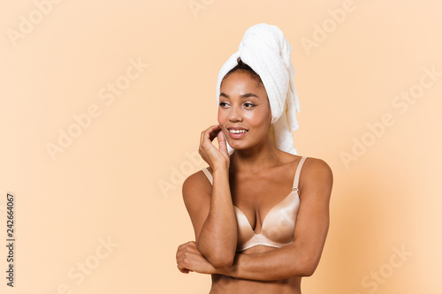 Portrait of smiling woman wrapped in towel and wearing white lingerie, standing isolated over beige background