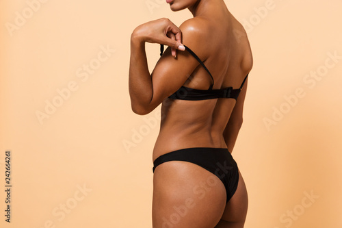 Photo of dark-skinned woman wearing black lingerie, standing isolated over beige background
