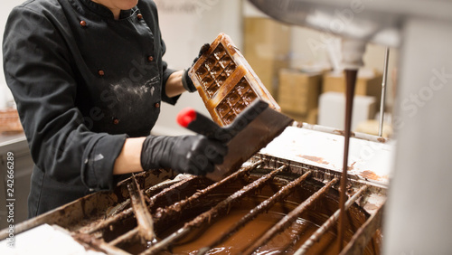 production, cooking and people concept - confectioner cleaning mold from extra chocolate by spatula at confectionery shop