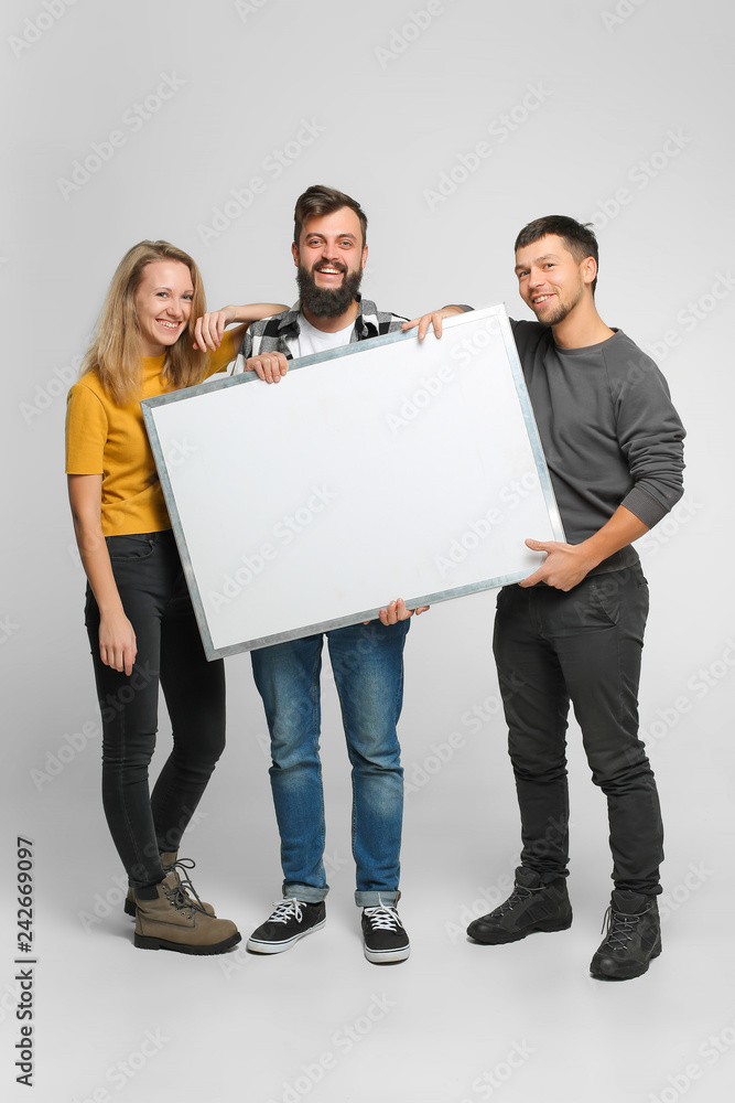 Portrait of three positive laughing young people wearing casual clothes, holding mockup white board isolated in studio, white background Portrait of three positive laughing young people wearing casual clothes, holding mockup white board isolated in studio, white background
