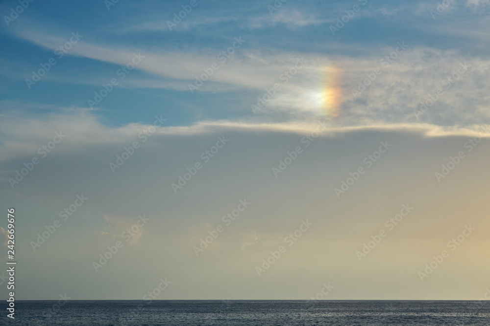 Blue cloudy sky with rainbow effect over the sea on a sunset as a natural background.