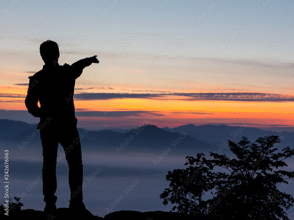 Silhouette of man standing on top mountain looks into the distance at morning misty landscape