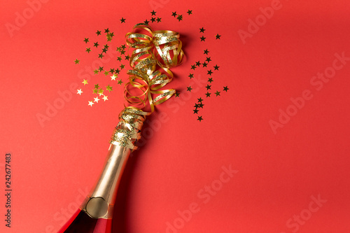 Champagne bottle wrapped in golden garland on red paper background. Valentines day, birthday, wedding celebration concept. Top view. Flat lay. Copy space. Toned