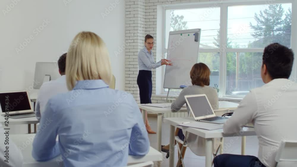 Young businesswoman drawing diagram on flipchart and explaining something to group of employees during seminar Young businesswoman drawing diagram on flipchart and explaining something to group of employees during seminar