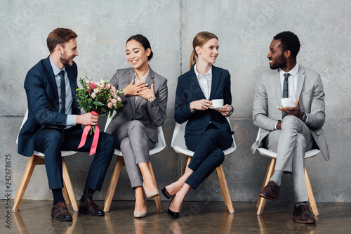 multiethnic businesspeople sitting with flowers and coffee in office