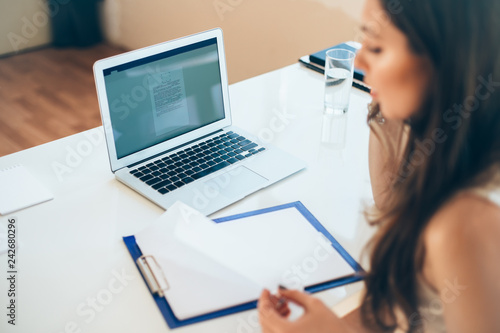 Young business woman sitting at table and reading documents at her workplace