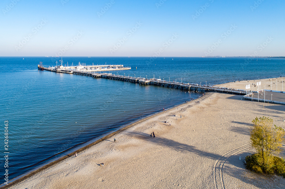 Wooden pier with harbor, pirate tourist ship, marina with yachts and beach in Sopot resort near Gdansk in Poland in sunset light. Aerial view