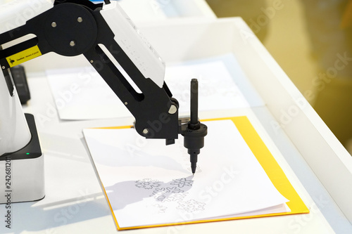 Photography Robotic hand with a pencil draws simple graphic drawings on white paper