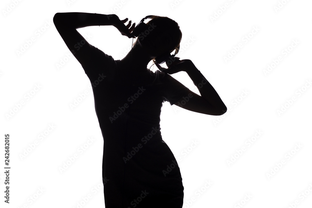 silhouette of a happy girl listening to music in headphones, figure of young woman with hands up relaxing on a white isolated background and and dancing to the music, concept of hobby and leisure