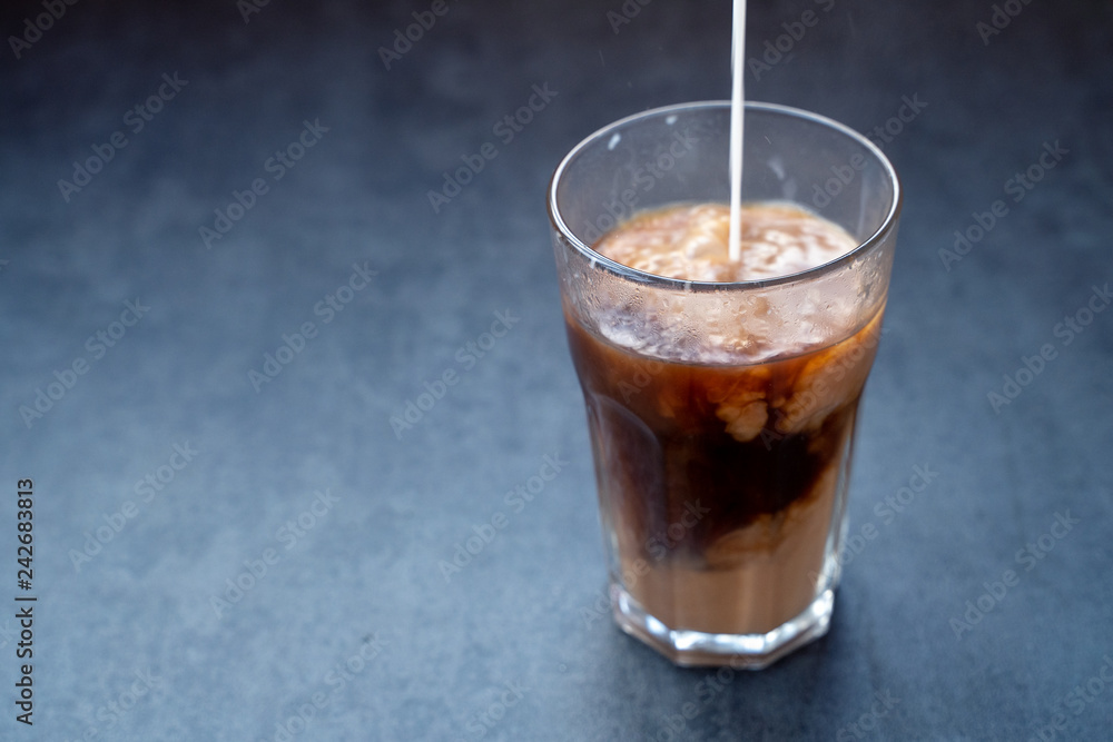 Pouring milk into coffee latte in the glass on a dark gray stone table, copy space. Pouring milk into coffee latte in the glass on a dark gray stone table, copy space.