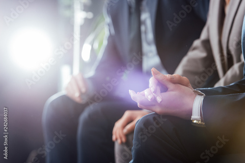 cropped view of businesswoman sitting with folded hands and colleague on background