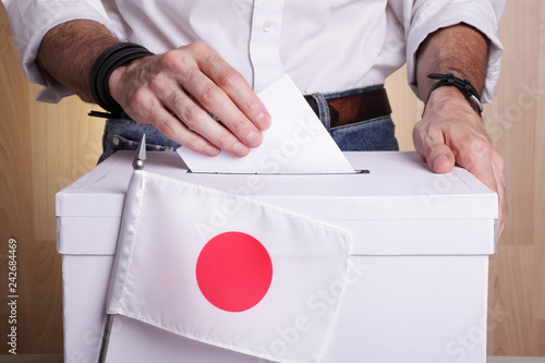 A Japanese citizen inserting a ballot into a ballot box. Japan flag in front of it photo