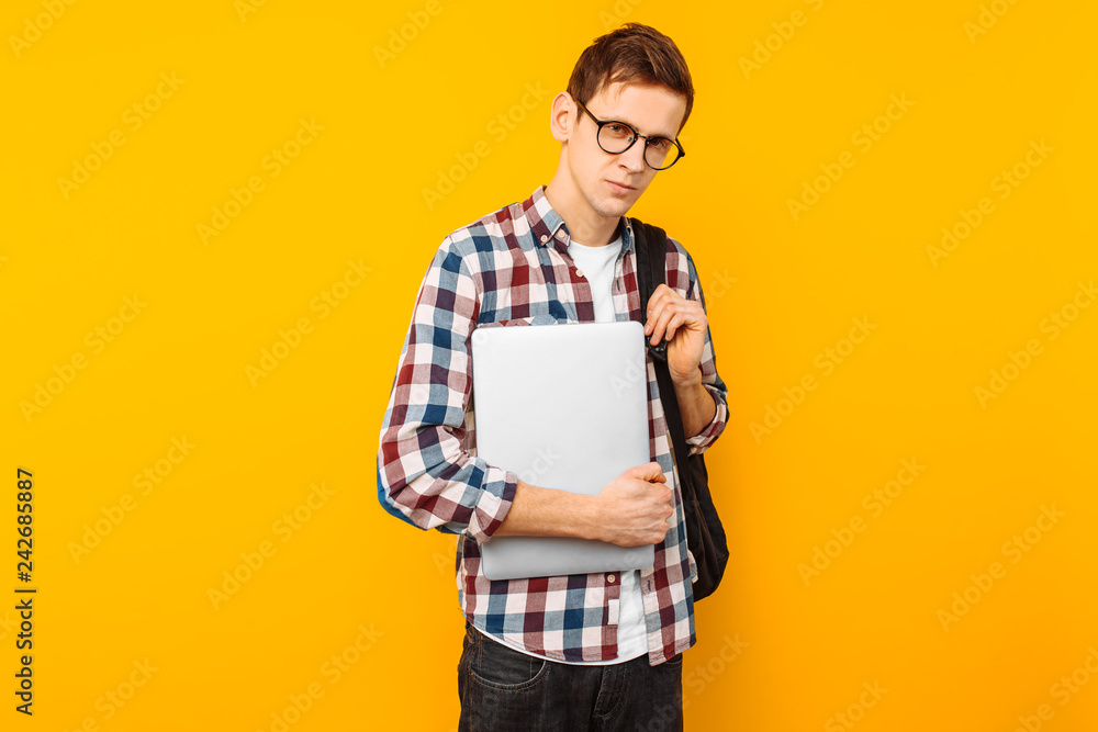 Happy guy with glasses, a man in a plaid shirt, with a closed laptop in hand, on a yellow background Happy guy with glasses, a man in a plaid shirt, with a closed laptop in hand, on a yellow background