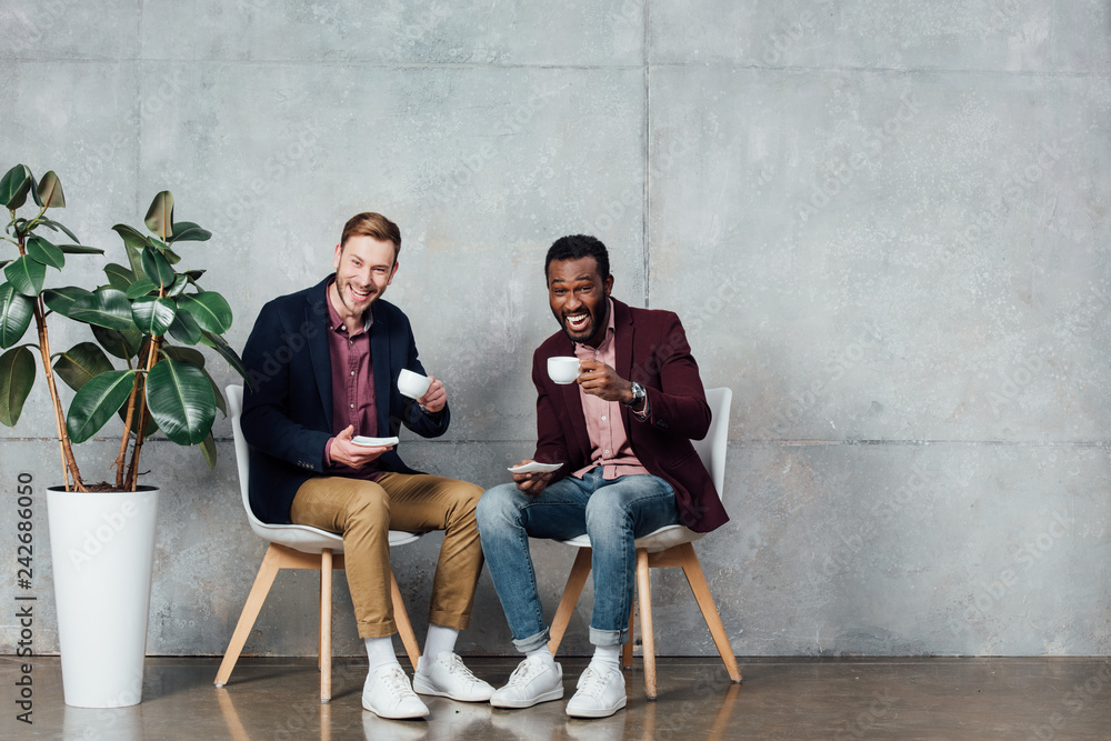 multiethnic men sitting, looking at camera and drinking coffee in waiting hall