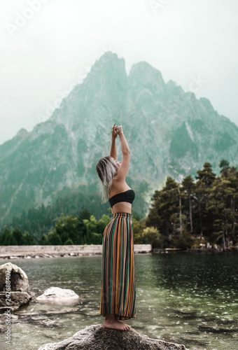 Side view of young woman standing on rock against lake and mountains