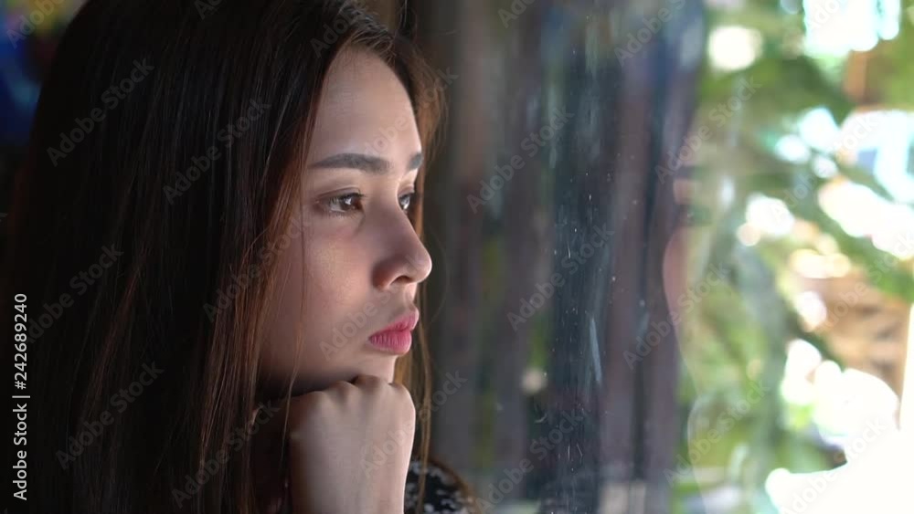 Close up serious young asian woman thinking and looking through window ...