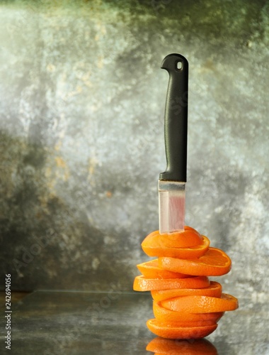 The orange is cut and stap by a old knife. on old glass desk in the kitchen room
