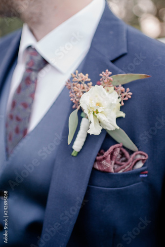 Groom in a suit with a tie and boutonniere. Flower design, floristry. Wedding day and accessories