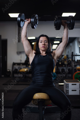 fitness girl trains with dumbbells in the gym. Pumps the deltoid muscles