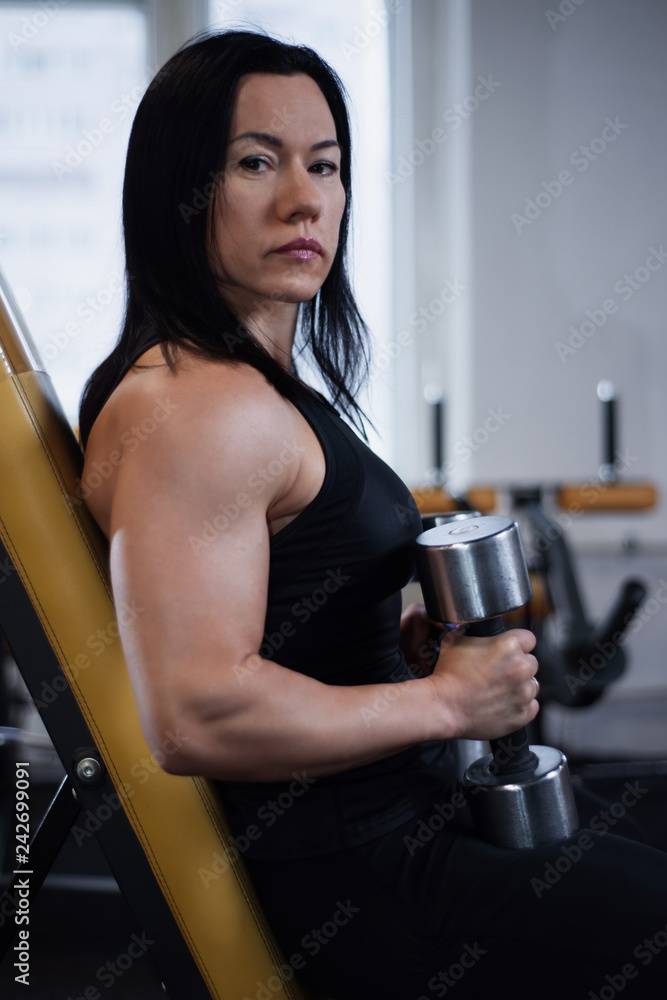 Fototapeta premium fitness girl trains with dumbbells in the gym. Resting between sets