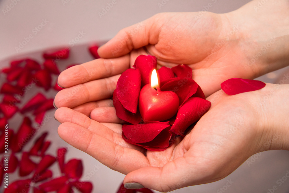 Valentines day surprise, close up woman holding red rose petals and hear candle in hands