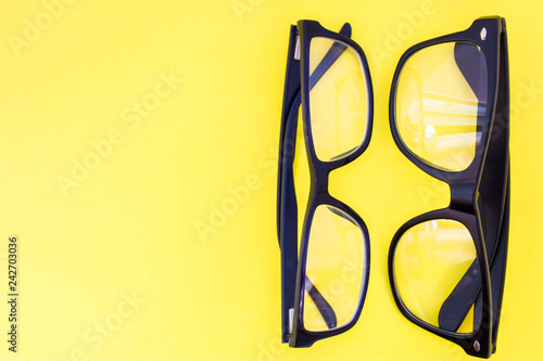 Two black eyeglasses on yellow uniform background view from above with the clear area of half photo for labels, headers. Concept photo of selection of glasses, optometrist work, shop of prescription