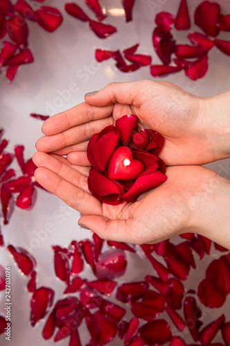 Valentines day surprise, close up woman holding red rose petals and hear candle in hands