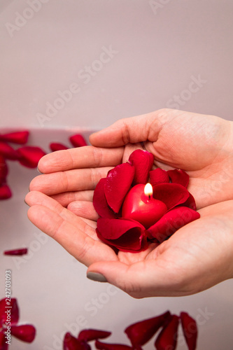 Valentines day surprise, close up woman holding red rose petals and hear candle in hands