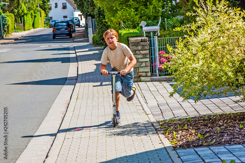 boy enjoys skating with his pust scooter at the sidewalk photo