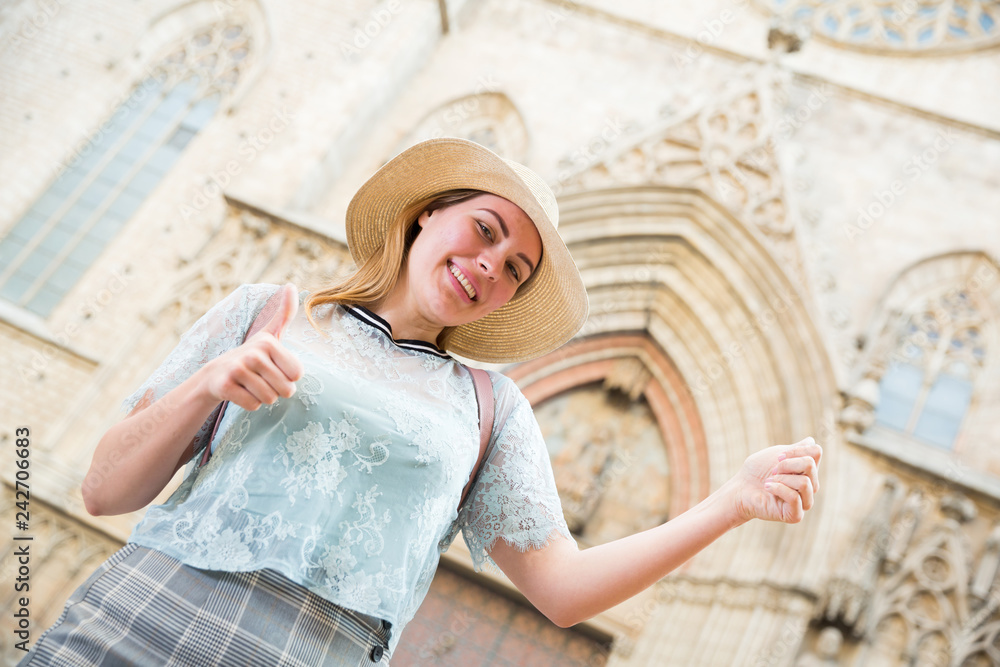 Young emotional woman in hat holding thumbs up in city center