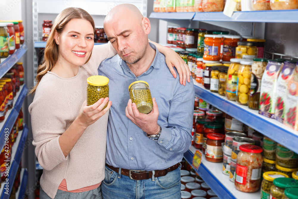 Positive family couple holding canned goods in the food store
