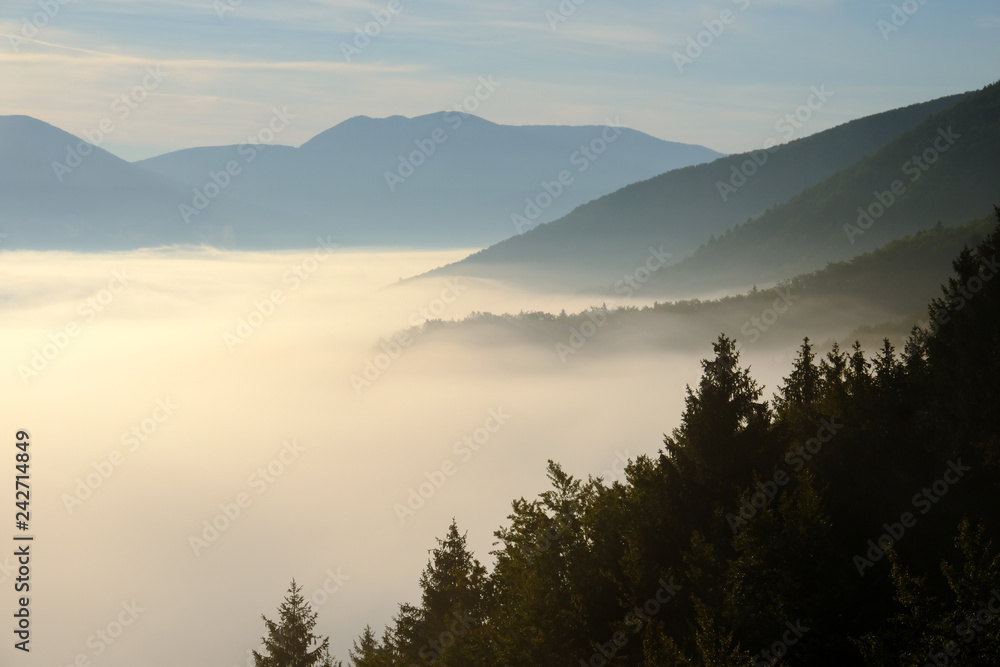 View above the clouds on the surrounding densly wooded hills