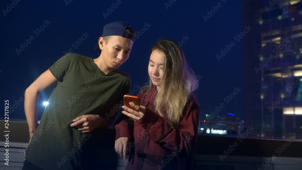 happy young asian couple boyfriend and girlfriend. use a smartphone while standing on a city street in the evening. happy young asian couple boyfriend and girlfriend. use a smartphone while standing on a city street in the evening.