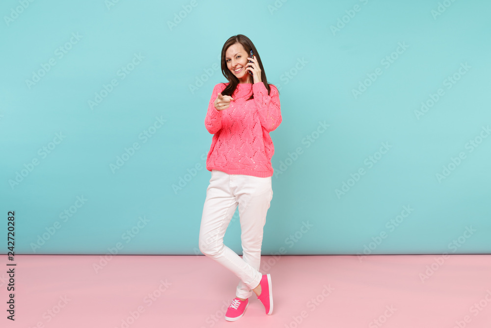 Full length portrait of woman in knitted rose sweater, white pants talking on mobile phone isolated on bright pink blue pastel wall background in studio. Fashion lifestyle concept. Mock up copy space. Full length portrait of woman in knitted rose sweater, white pants talking on mobile phone isolated on bright pink blue pastel wall background in studio. Fashion lifestyle concept. Mock up copy space.