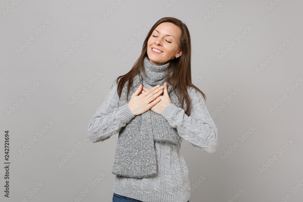 Pleasant young woman in gray sweater, scarf with closed eyes holding hands crossed on chest isolated on grey wall background. Healthy fashion lifestyle, people sincere emotions, cold season concept. Pleasant young woman in gray sweater, scarf with closed eyes holding hands crossed on chest isolated on grey wall background. Healthy fashion lifestyle, people sincere emotions, cold season concept.