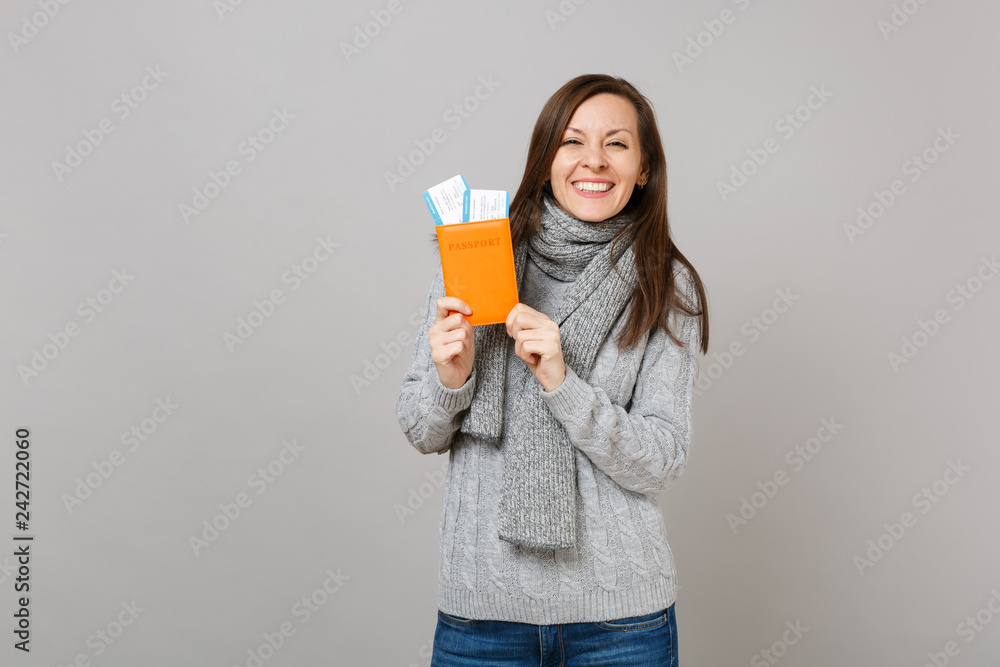 Joyful young woman in gray sweater, scarf holding passport boarding pass ticket isolated on grey background. Healthy fashion lifestyle people sincere emotions, cold season concept. Mock up copy space. Joyful young woman in gray sweater, scarf holding passport boarding pass ticket isolated on grey background. Healthy fashion lifestyle people sincere emotions, cold season concept. Mock up copy space.